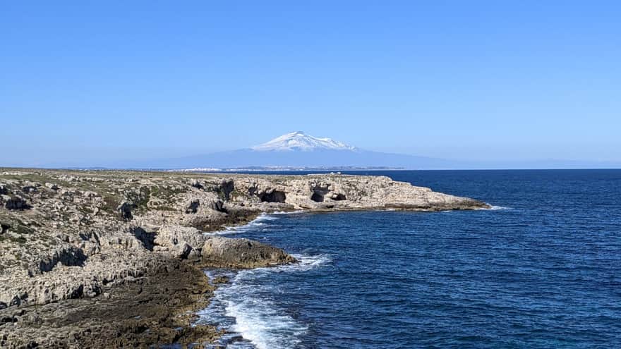 Rocky coast towards the town of Targia with a view of Mount Etna