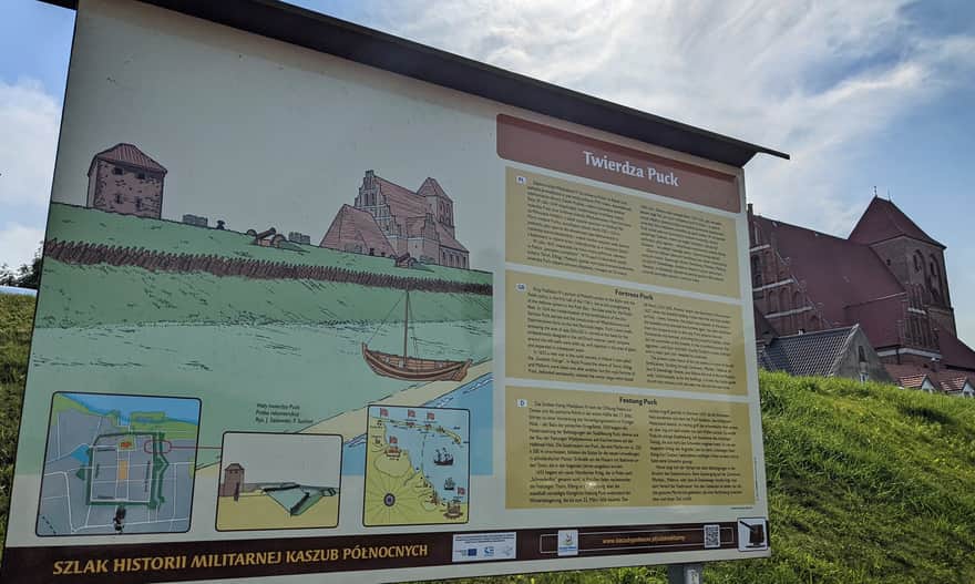 Puck Fortress - information board at the Puck port. In the background, the Gothic Church of St. Peter and Paul.
