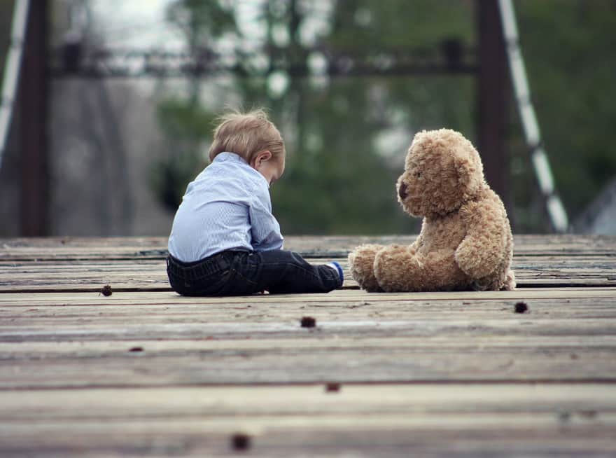 Chłopiec siedzi na drewnianym podeście w towarzystwie pluszowego misia.